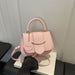 A light pink faux leather handbag with a top handle, a circular 'FASHION' tag, and a gold-tone curved accent on the front, resting on a white box with a black sleeve holding the strap.