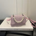 A small pink textured handbag with a pearl beaded strap, resting on a white book.