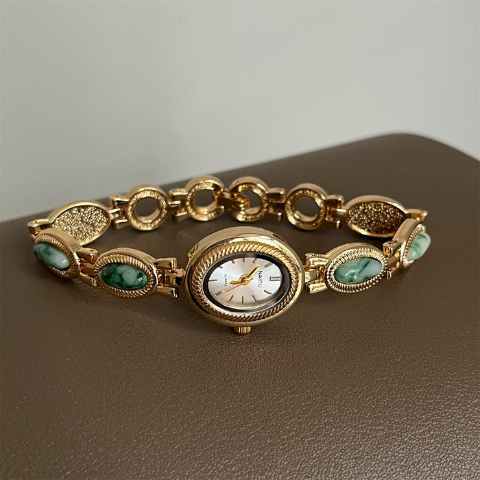 Gold bracelet watch with green gemstones on a brown surface
