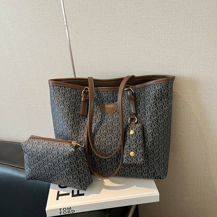 A dark gray and brown monogram tote bag with matching zip pouch, displayed on a white book against a beige textured wall.