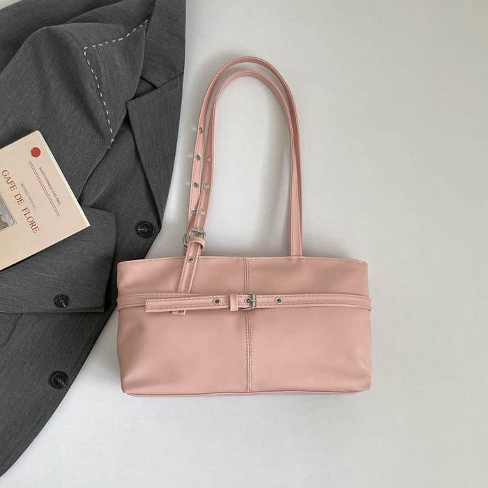 A light pink faux leather tote bag with double shoulder straps and silver-tone hardware, styled on a light gray surface next to a dark gray blazer and a book.