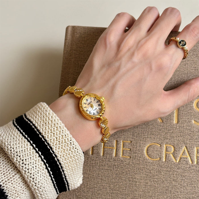 Hand wearing a gold watch with a textured sleeve on a beige surface