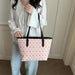 A person wearing a white lace blouse and light blue jeans carries a large light pink tote bag with a repeating monogram pattern and black shoulder straps in an indoor setting.
