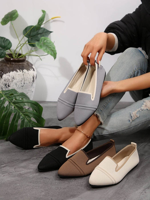 Person holding a gray flat shoe with other colored flats on a gray surface.