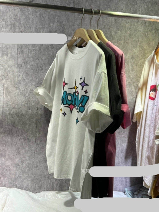 White t-shirt with colorful text design on a rack against a gray wall.