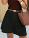 Person wearing a brown top and black shorts with a brown belt, holding a brown handbag.