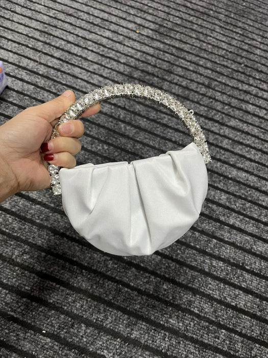 White handbag with a decorative handle held by a hand on a textured surface