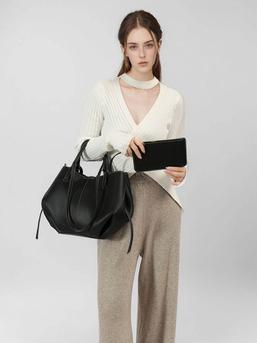 Woman holding a black handbag and clutch against a plain background