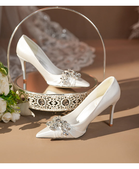 White high-heeled shoes with decorative embellishments on a reflective surface.