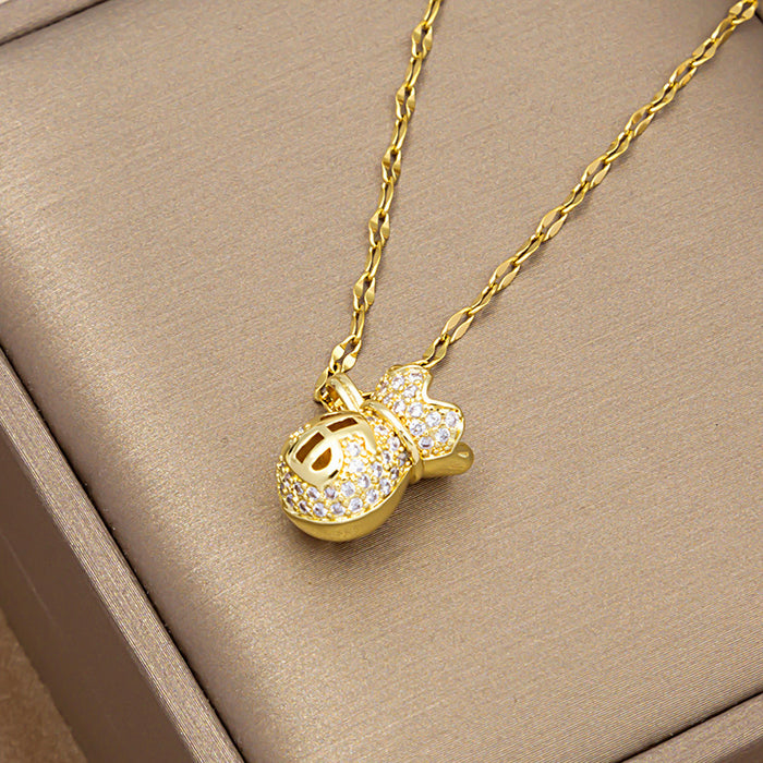 A gold chain necklace with a money bag pendant, heavily embellished with clear crystals, resting on a textured beige jewelry box.