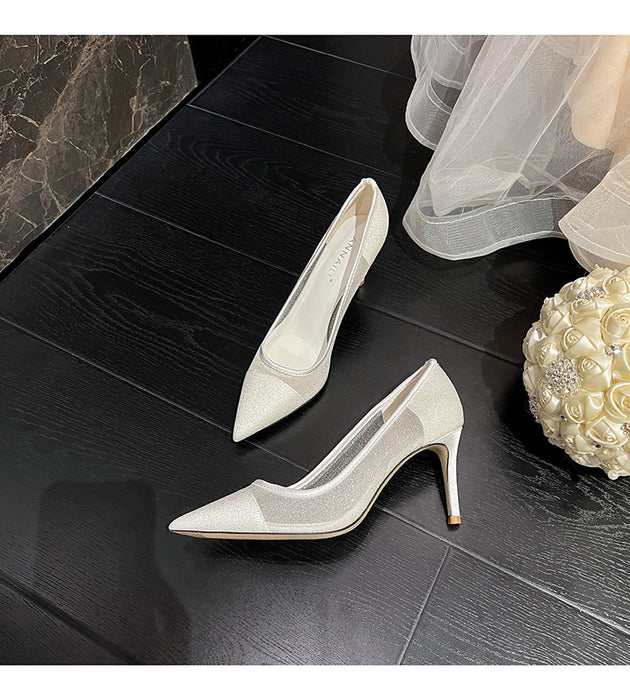 White high-heeled shoes on a dark wooden floor with a decorative flower arrangement.