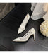White high-heeled shoes on a dark wooden floor with a decorative flower arrangement.