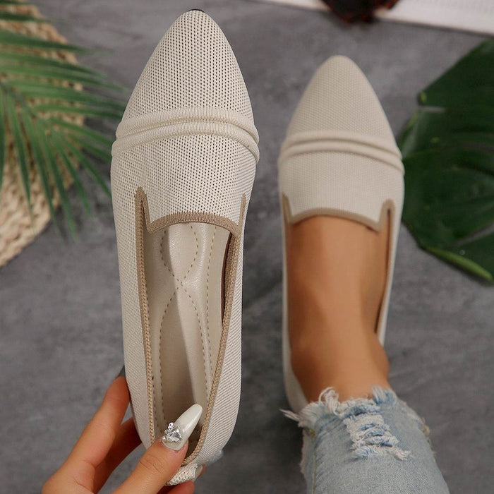 Beige pointed-toe flats held by a hand with a blurred background