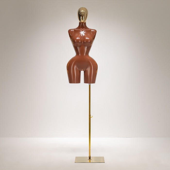 Mannequin torso on a stand with a gold head and base against a neutral background