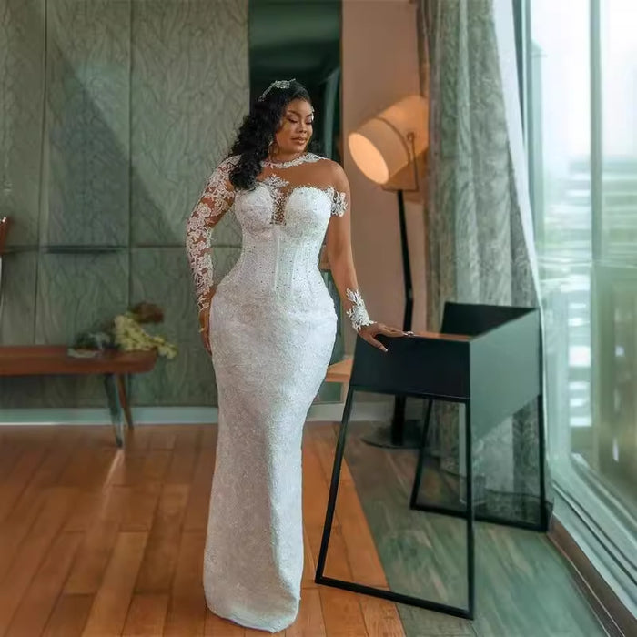 Woman in a white lace dress standing in a modern room with large windows.
