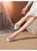 White high-heeled shoes with embellishments worn by a person in a white dress against a blurred background.