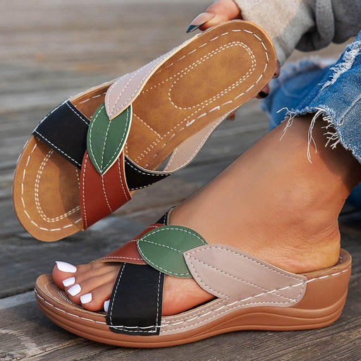 Colorful sandals with leaf patterns worn by a person on a wooden surface