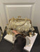 A gold-tone kiss-lock handbag covered in round metallic coin embellishments and hanging clear beads, held by a person wearing a black sleeveless top. The bag is displayed on a white book on a black table in front of a white paneled wall.