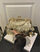 A gold-tone kiss-lock handbag covered in round metallic coin embellishments and hanging clear beads, held by a person wearing a black sleeveless top. The bag is displayed on a white book on a black table in front of a white paneled wall.