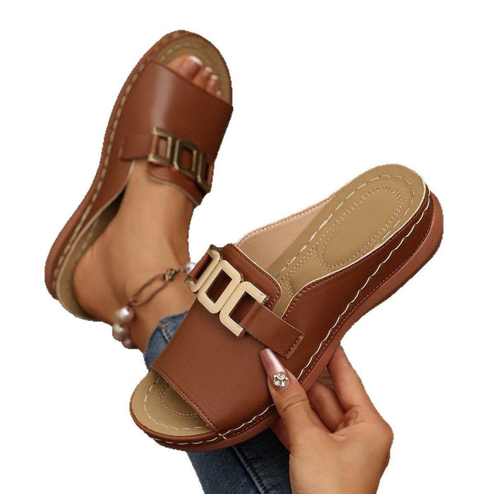 Brown sandals with gold buckles held by a hand on a white background