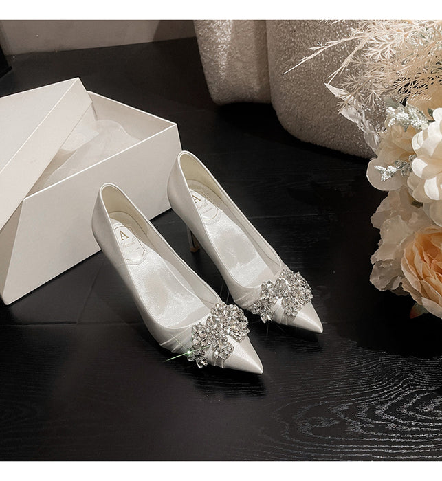 White wedding shoes with decorative embellishments on a dark surface next to a white box and floral arrangement.