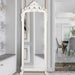 White ornate full-length mirror in a room with gray walls and a dining area.
