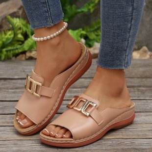 Brown sandals with gold buckles worn by a person on a wooden surface.