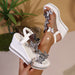 White wedge sandals with butterfly embellishments held by a hand against a blurred indoor background.