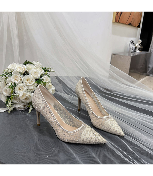 Pair of silver high-heeled shoes with a bouquet of white roses on a draped fabric background