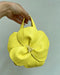 Yellow flower-shaped handbag held by a hand against a light gray background