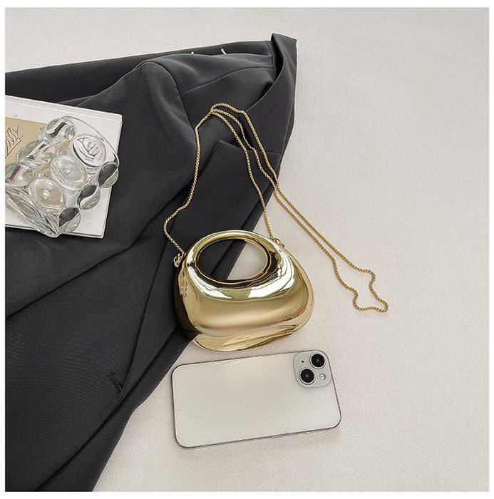 Gold handbag with a chain strap on a light gray surface with a black fabric background.