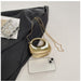 Gold handbag with a chain strap on a light gray surface with a black fabric background.