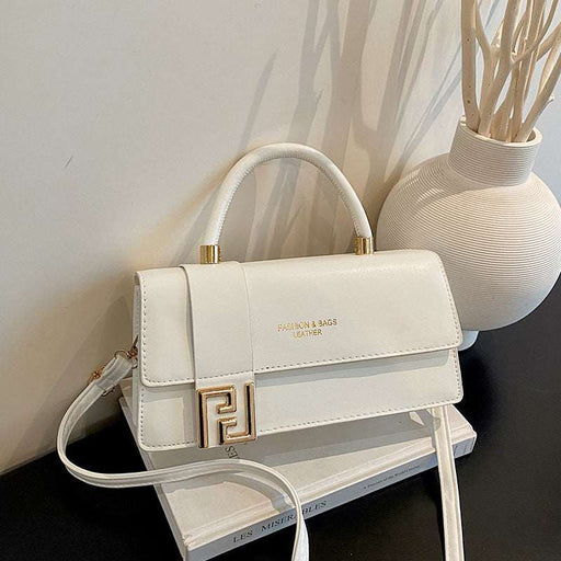 A white faux leather handbag with a gold-tone FF logo clasp and top handle, resting on a white book next to a textured white vase.