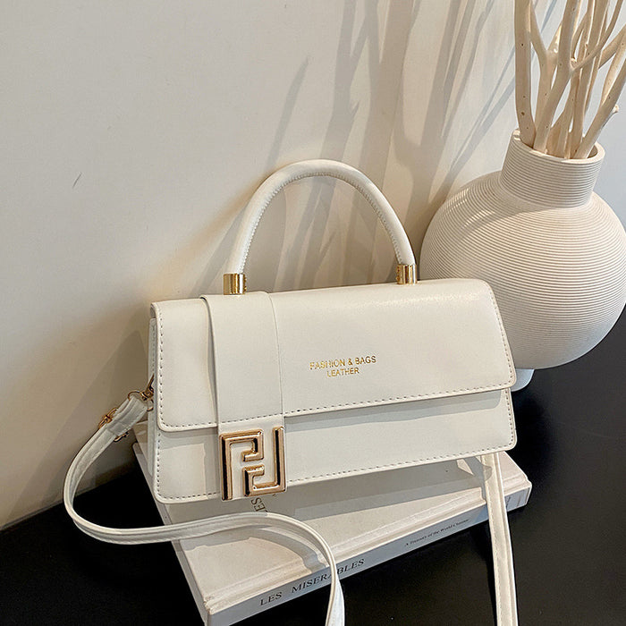 A white faux leather handbag with a gold-tone FF logo clasp and top handle, resting on a white book next to a textured white vase.
