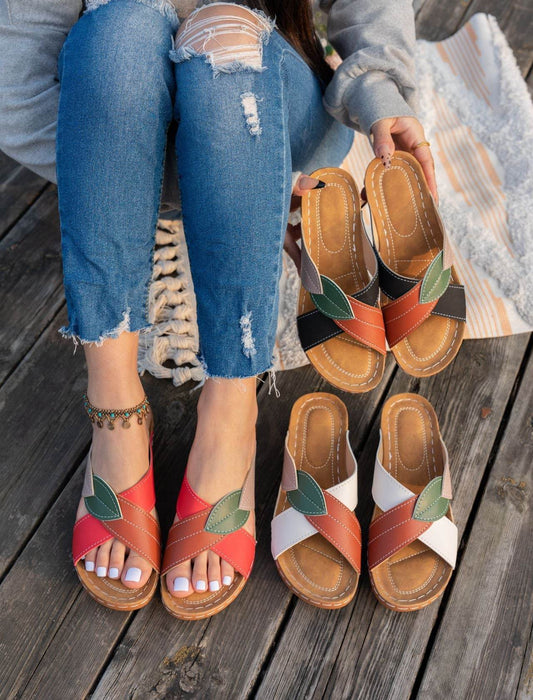 Colorful sandals with leaf designs worn by a person on a wooden floor.