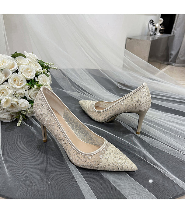 Pair of glittery high-heeled shoes on a tulle fabric with white roses.