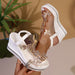 White wedge sandals with gold embellishments held by a hand against a neutral background
