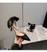 Black high-heeled shoe with bow and pearl details held by a hand on a marble surface.