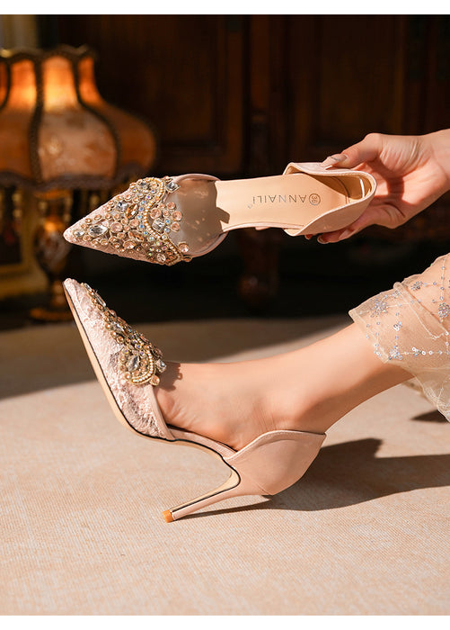 Beige high-heeled shoes with embellishments being worn, held by a hand.