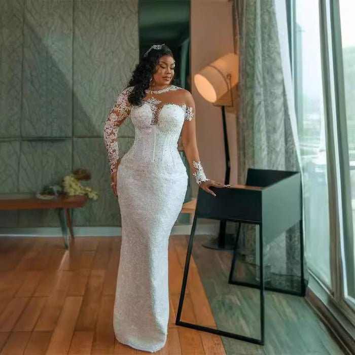 Woman in a white lace dress standing in a modern room with large windows.