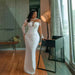 Woman in a white lace dress standing in a modern room with large windows.