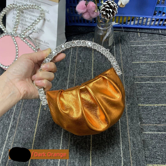 Gold handbag with decorative handle held by a hand on a textured surface.