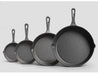 Set of four cast iron skillets of different sizes on a light gray background