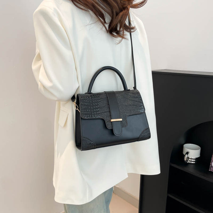 A woman wearing a white blazer carries a black crocodile-embossed top-handle handbag with a shoulder strap and gold-tone hardware.