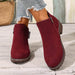 Red suede ankle boots worn with denim jeans on a wooden floor.