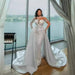 Woman in a white wedding dress standing in a room with large windows.