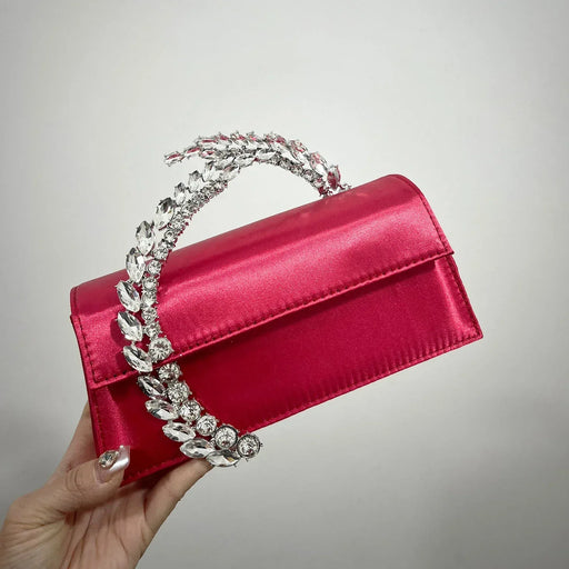 Red handbag with a decorative handle held by a hand against a gray background
