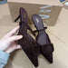 Brown pointed-toe shoes with a bow held by a hand, with a box in the background.