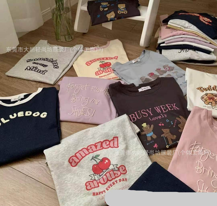 Various folded t-shirts with different designs and text on a wooden floor.