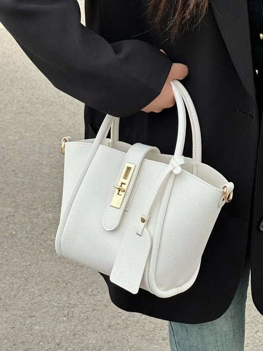 White handbag with gold accents held by a person wearing a black coat.